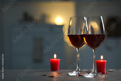 Glasses of red wine and burning candles on grey table against blurred lights, space for text. Romantic atmosphere
