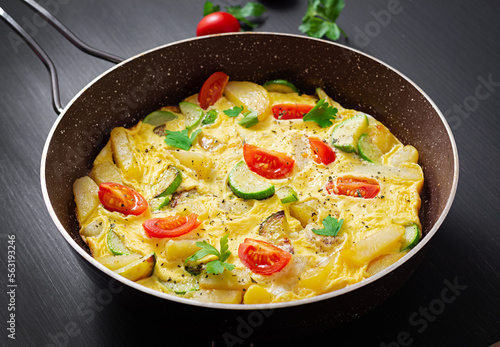 Omelette with tomatoes,  zucchini and potatoes on dark background. Healthy diet food for breakfast. Tasty morning food.