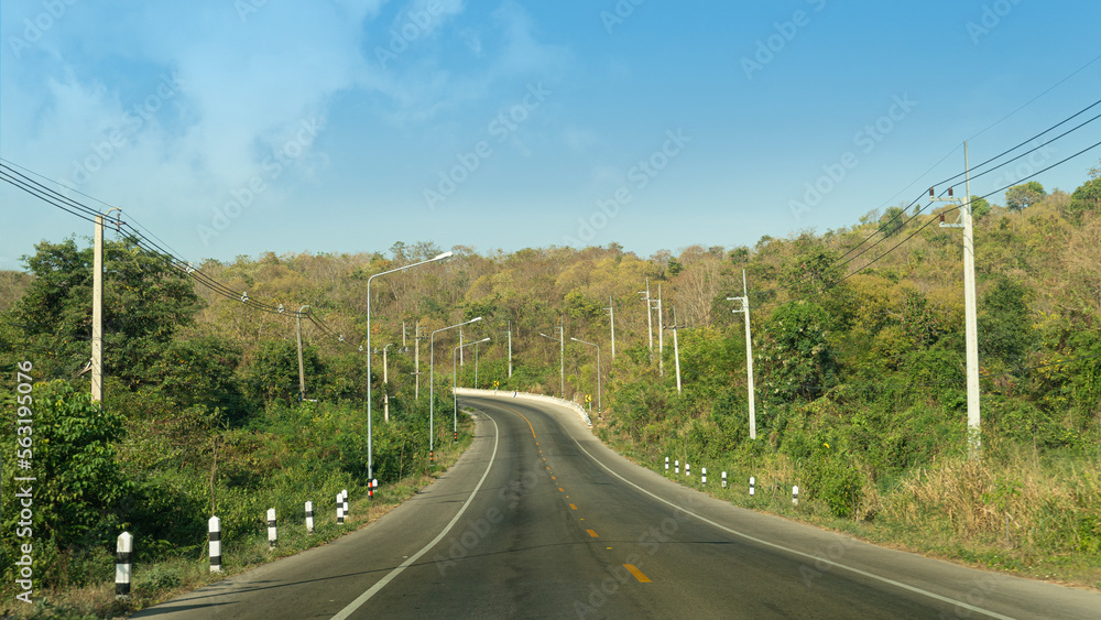 Traffic route of asphalt road that goes straight up the mountain and curvy path. On both sides of the road there are electric poles lined up. Background of mountain under the blue sky. Traffic route of asphalt road that goes straight up the mountain and curvy path. On both sides of the road there are electric poles lined up. Background of mountain under the blue sky.