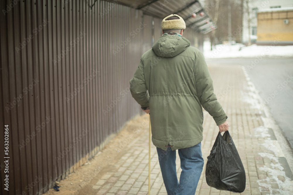 Old man walks with bag of groceries. Pensioner in Russia. Man walks down street.