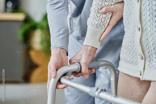 Close-up of caregiver helping senior woman to walk using walker
