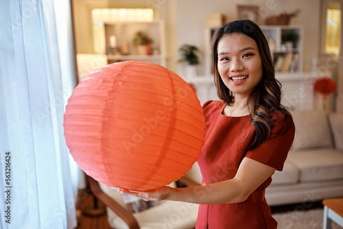Happy Chinese woman holding red lantern at home and looking at camera.