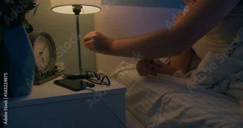 Young man put off eyewear and swith off light on nightstand and goes to sleep at night, medium close-up shot