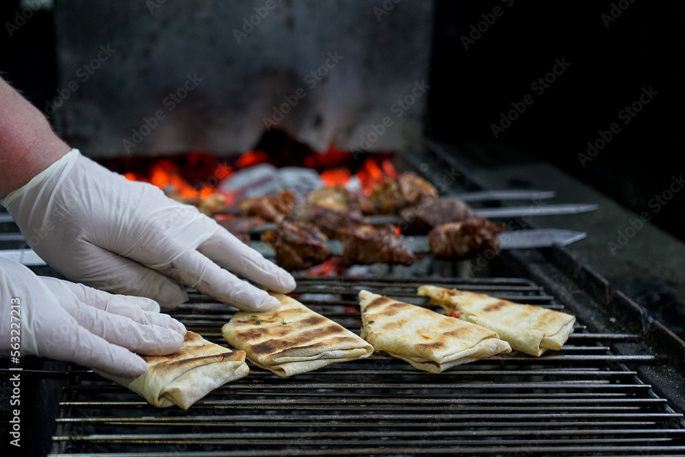 meat kebab on skewers on a grill is fried with pita bread on coals with fire
