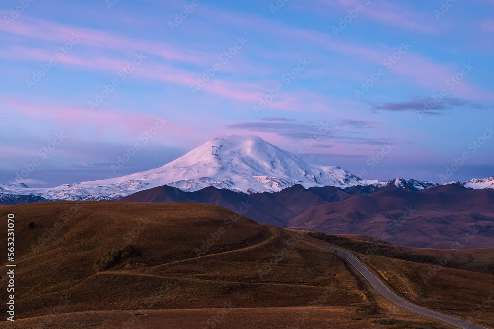 Purple twilight with snow-capped mountain top and highway through autumn valley.