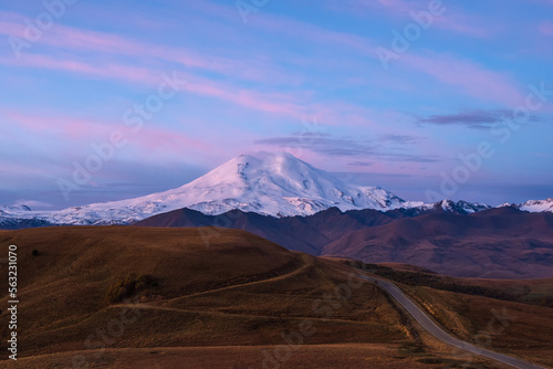 Purple twilight with snow-capped mountain top and highway through autumn valley.