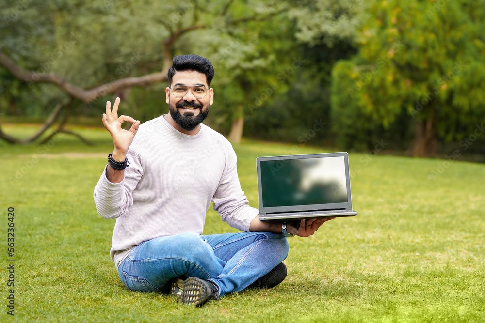 Obraz premium Young indian man showing laptop screen at park.