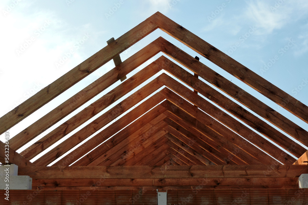 A timber roof truss of a house under construction, reinforced brick lintels, blue sky in the background A timber roof truss of a house under construction, reinforced brick lintels, blue sky in the background