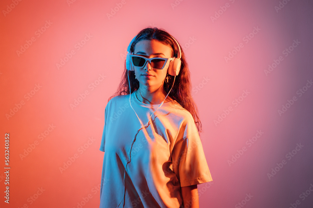 Stylish teen hipster pretty fashion girl model wear glasses and headphones, enjoy and listen new dance music looking at camera at colorful studio background. Stylish teen hipster pretty fashion girl model wear glasses and headphones, enjoy and listen new dance music looking at camera at colorful studio background.