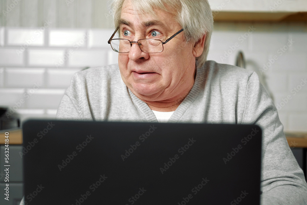 Senior grey haired man wearing glasses sitting at laptop and making fish face with lips. Crazy and comical gesture. Funny Old grandfather with playful silly facial expression grimacing fooling around Senior grey haired man wearing glasses sitting at laptop and making fish face with lips. Crazy and comical gesture. Funny Old grandfather with playful silly facial expression grimacing fooling around