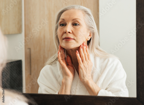 Senior woman stretching skin on her face in front of a mirror