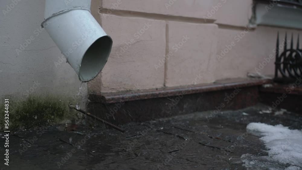 Melting water splashing from steel drainpipe mounted on building wall outdoor. Sewerage urban system in spring season. Melting water splashing from steel drainpipe mounted on building wall outdoor. Sewerage urban system in spring season.