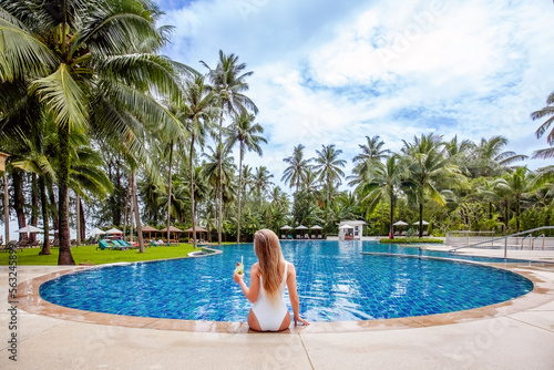 Back view of travel woman influencer with tropical cocktail sitting in swimming pool