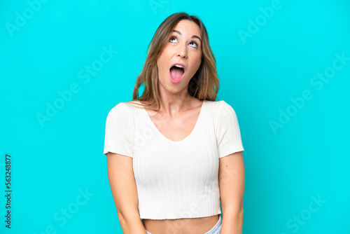 Young caucasian woman isolated on blue background looking up and with surprised expression