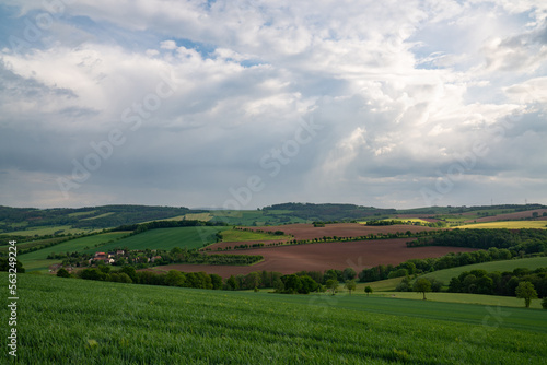 Hilly area in Saxony, near Dresden. Landscape with green fields and meadows. Houses are visible in the distance. Dark sky and many clouds. Before sunset. © Alexander