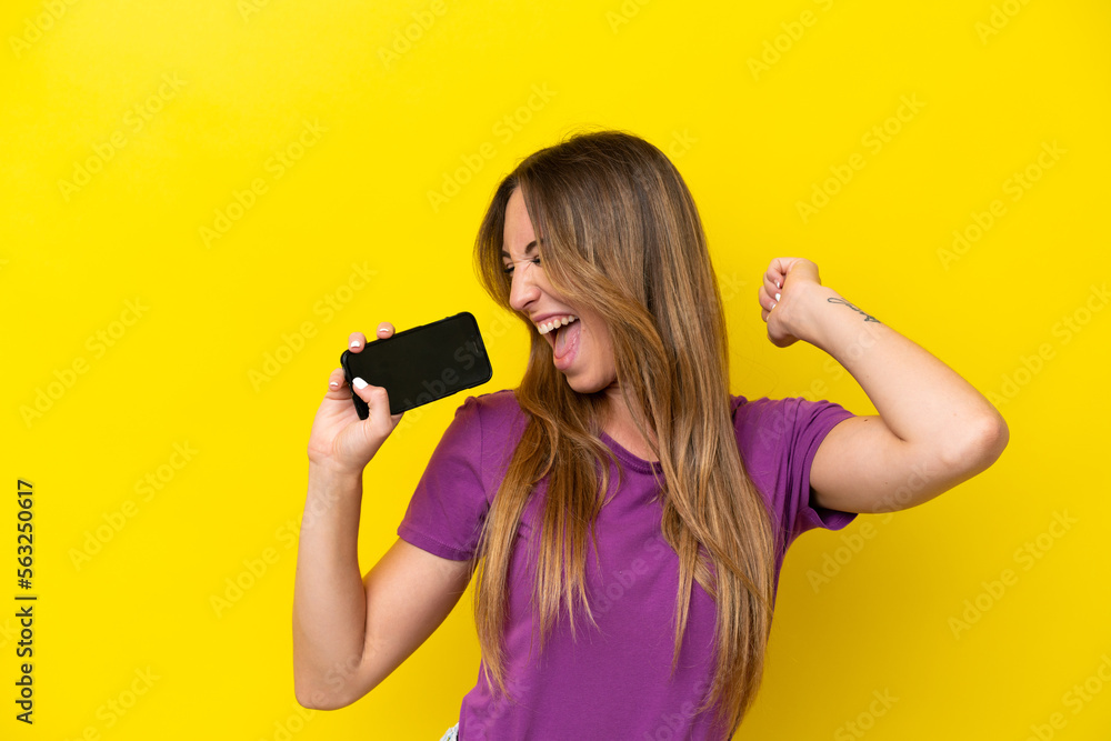 Young caucasian woman isolated on yellow background using mobile phone and singing Young caucasian woman isolated on yellow background using mobile phone and singing