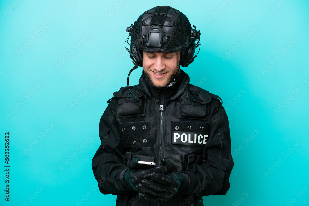 SWAT caucasian man isolated on blue background sending a message with the mobile SWAT caucasian man isolated on blue background sending a message with the mobile