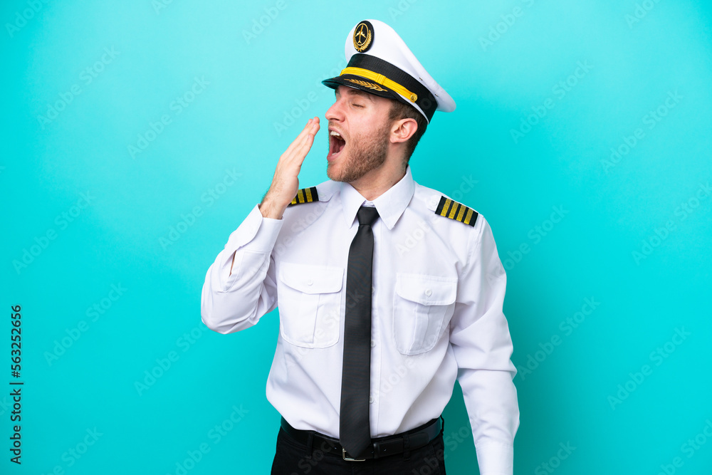 Airplane caucasian pilot isolated on blue background yawning and covering wide open mouth with hand