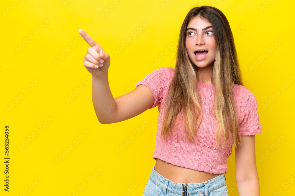 Young caucasian woman isolated on yellow background pointing away