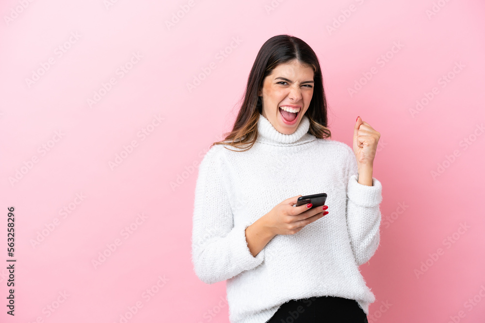 Young Italian woman isolated on pink background with phone in victory position Young Italian woman isolated on pink background with phone in victory position