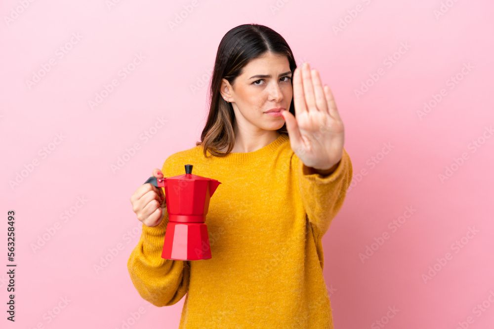 Young Italian woman holding a coffee maker isolated on pink background making stop gesture Young Italian woman holding a coffee maker isolated on pink background making stop gesture