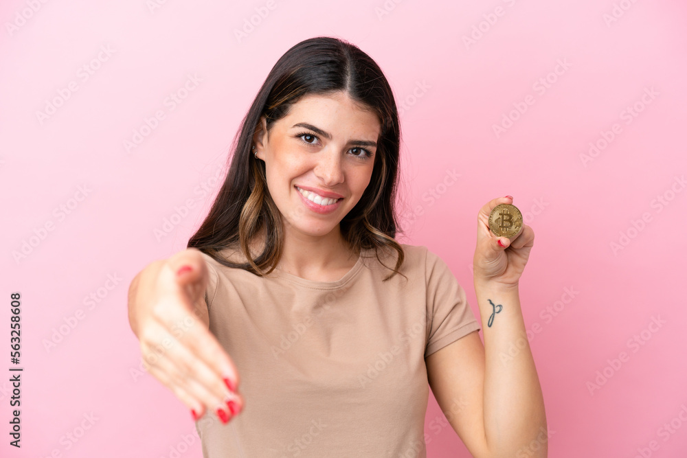 Young Italian woman holding a Bitcoin isolated on pink background shaking hands for closing a good deal Young Italian woman holding a Bitcoin isolated on pink background shaking hands for closing a good deal