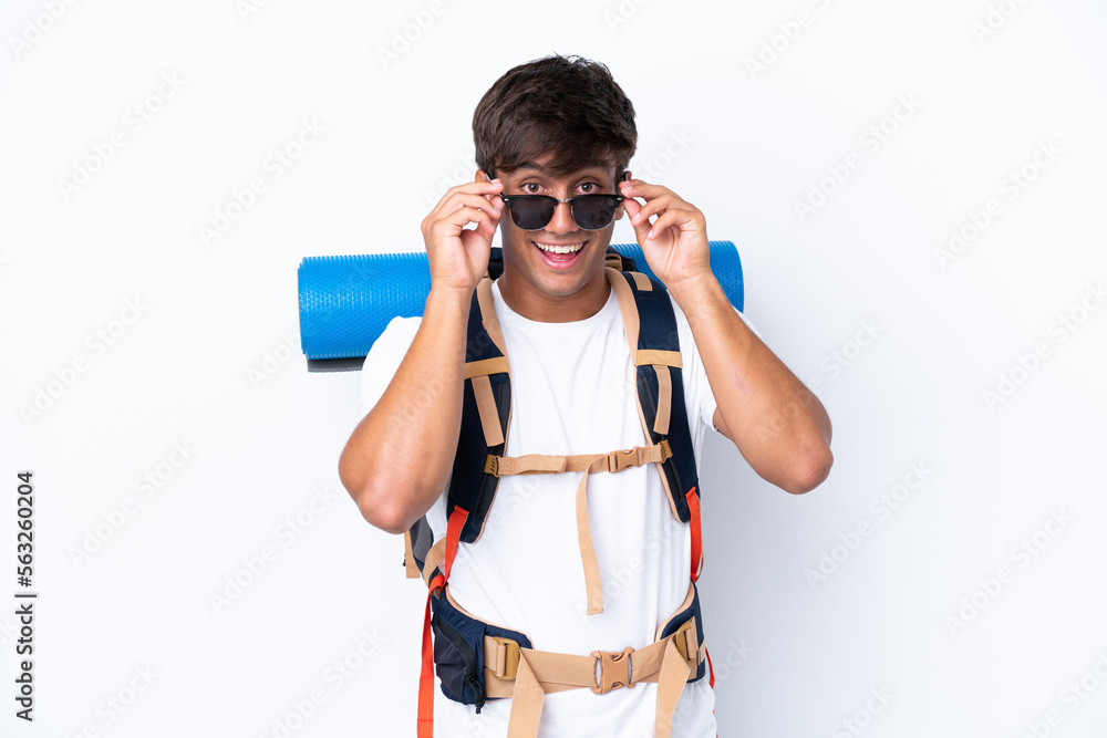 Young mountaineer woman with a big backpack over isolated white background with glasses and surprised Young mountaineer woman with a big backpack over isolated white background with glasses and surprised