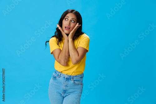 Woman in yellow t-shirt on blue background posing gestures emotions and signals with smile, hands up happiness copy space