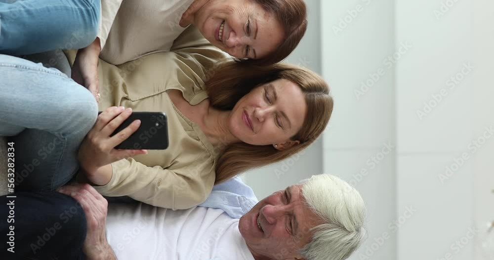 Cheerful positive engaged old parents and pretty adult daughter taking video selfie, making group call, watching media content, online ecommerce app, using smartphone for communication Cheerful positive engaged old parents and pretty adult daughter taking video selfie, making group call, watching media content, online ecommerce app, using smartphone for communication