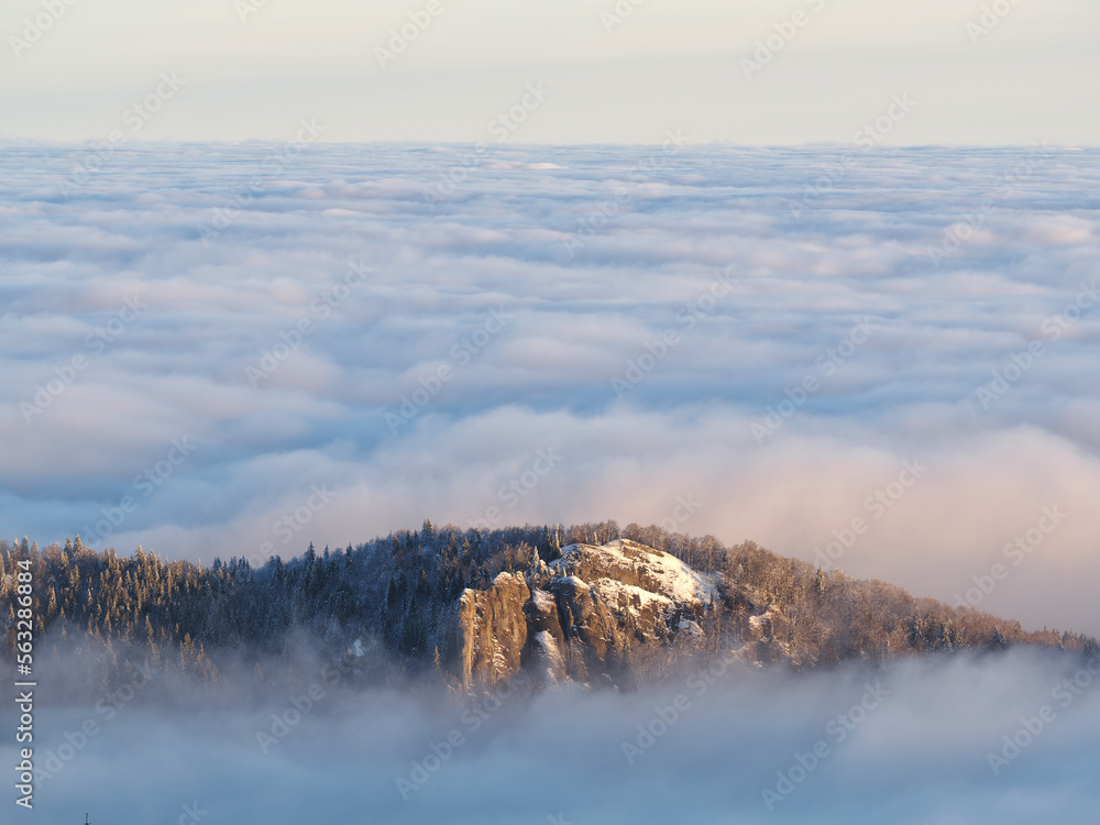 Obraz premium Aerial view of distant mountain peaks above clouds in clear sunny blue sky.