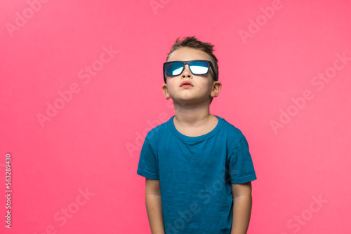 Little boy in sunglasses posing in studio on pink background. Copy space