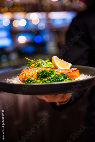 Fototapeta Naklejka Na Ścianę i Meble -  waiter hand with plate of Fried salmon with creamy sauce, broccoli and salad