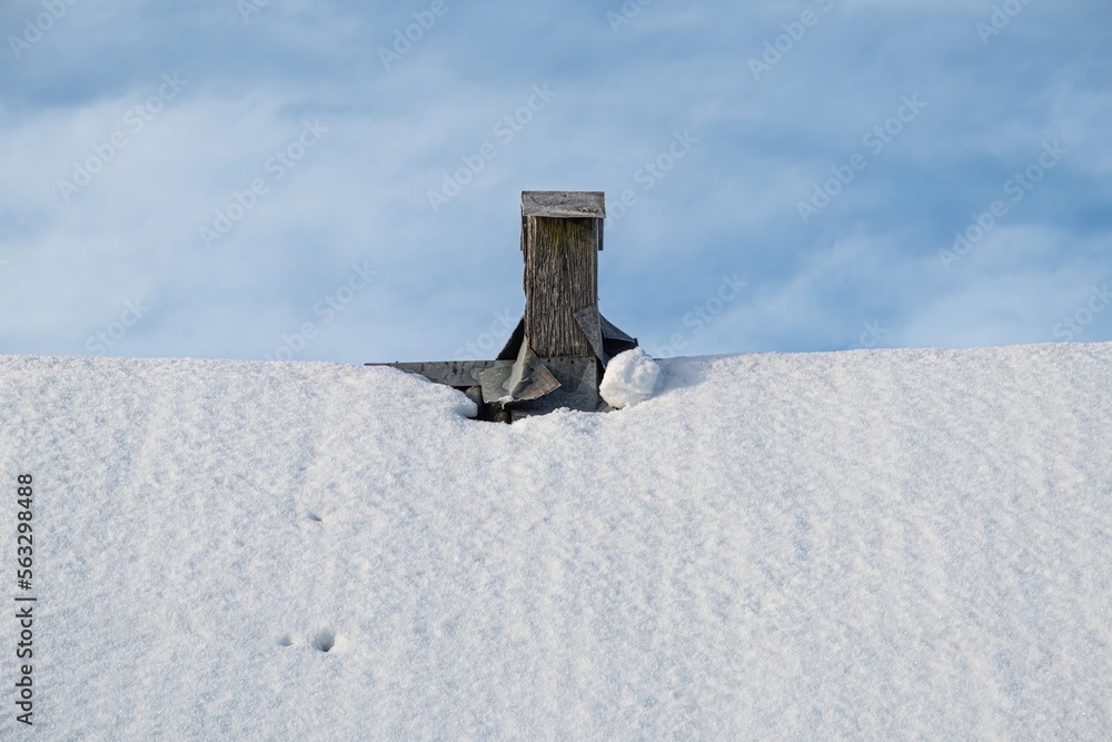 Fototapeta premium The roof is covered with snow, with a wooden chimney and a blue sky with clouds.