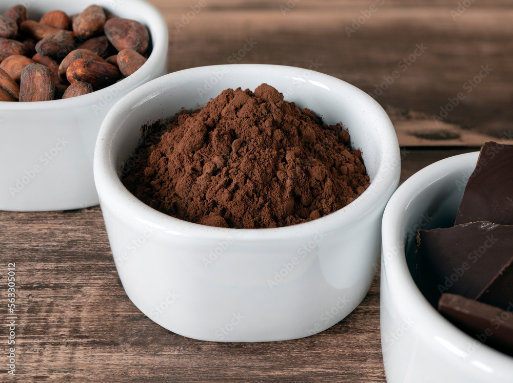 Cocoa powder in the bowl and other chocolate products on the wooden table. Cacao powder, cocoa beans and dark chocolate Cocoa powder in the bowl and other chocolate products on the wooden table. Cacao powder, cocoa beans and dark chocolate