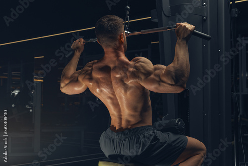 Bodybuilder in gym. Muscular man working out in gym, doing exercise back lat pulldown. Strong male rear view