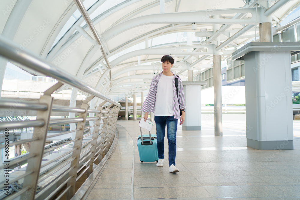 Happy cheerful Asian handsome young man walking in the city railway station alone with suitcase. Happy cheerful Asian handsome young man walking in the city railway station alone with suitcase.