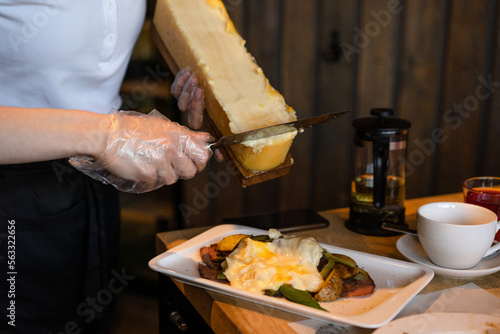 Bilde på lerret The waiter cuts the cheese into a raclette with a knife