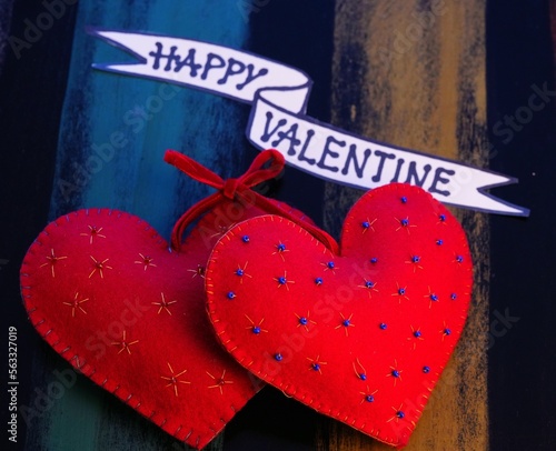 valentinstag, 2 rote herzen aus gewalkter wolle, prall gefüllt und verziert auf einer bunten truhe, schriftzug 