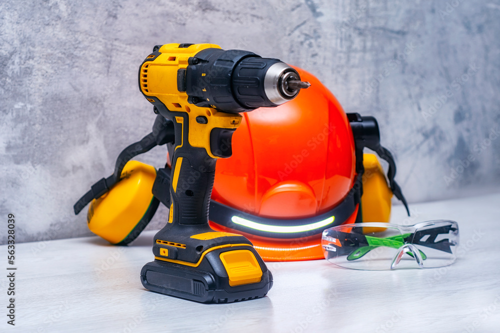 Electric screwdriver and a construction safety helmet for a head with an earpiece and a headlamp on the table. Construction tool and form for protection.