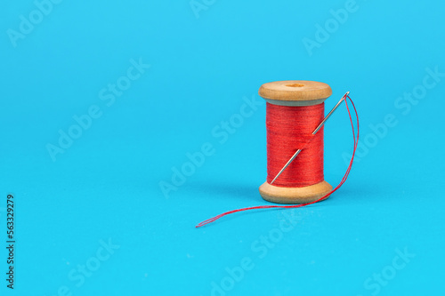 Spool of red thread with a needle on a blue background