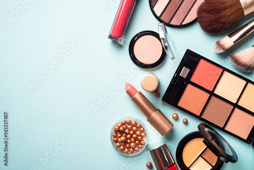 Make up professional cosmetics on blue background. Powder, lipstick, shadow, brushes with green leaves. Flat lay with copy space.