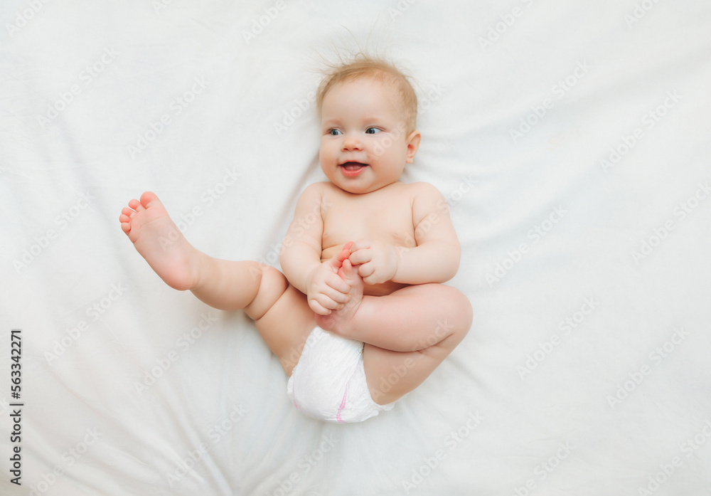 a happy joyful baby in diapers is lying on a white bed and holding his leg. High-quality photo. place for text a happy joyful baby in diapers is lying on a white bed and holding his leg. High-quality photo. place for text