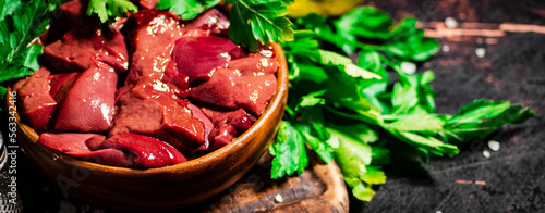 Pieces of raw liver in a bowl on a parsley cutting board.