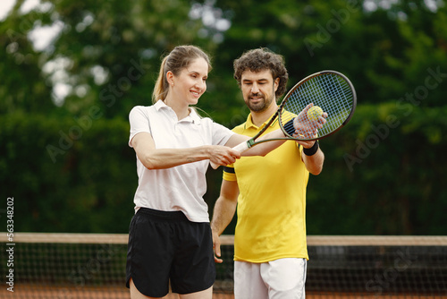 Curly man teaches a woman to play tennis on the open tennis court