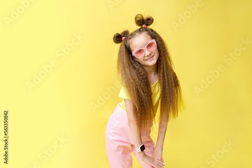Cool cute girl with a trendy hairstyle and pink sunglasses with bright emotionson a yellow background