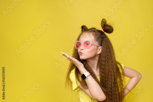 Cool cute girl with a trendy hairstyle and pink sunglasses with bright emotionson a yellow background