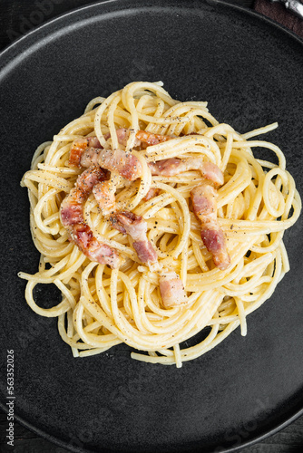 Traditional italian dish spaghetti carbonara with bacon in a cream sauce, on black wooden background, top view flat lay