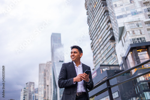 A portrait of a young smiling, happy, successful business man, executive walking outside down the street using mobile phone. 