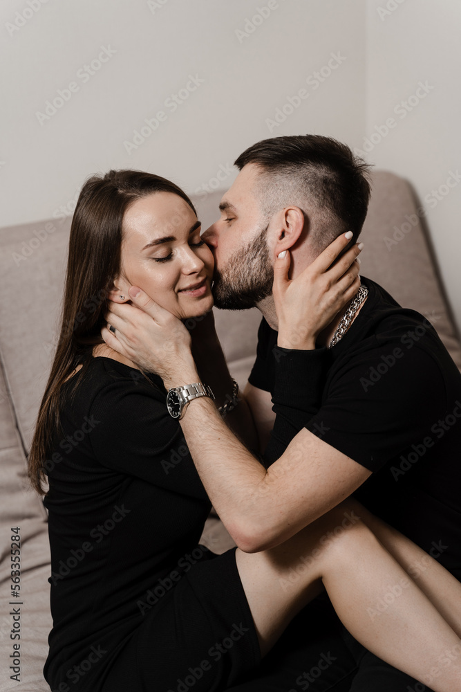 Love story of a couple spending time in cozy room at home. Relationships, feelings and tenderness in the family of men and girl. Couple in love hugging and kissing on couch at home.