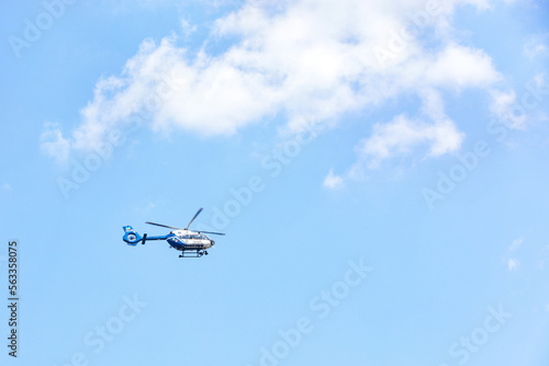 A flying police helicopter against a blue sky and a white cloud.